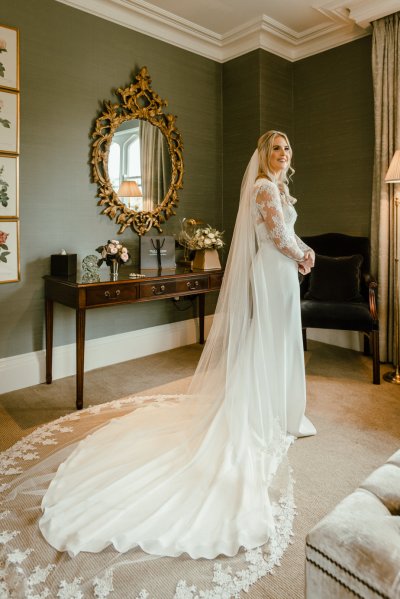 Bride standing mirror in background on sofa couch smiling train veil