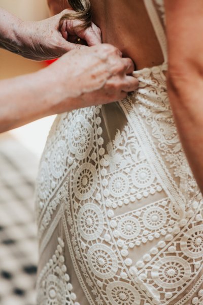 Bridesmaid helping bride button up lace dress