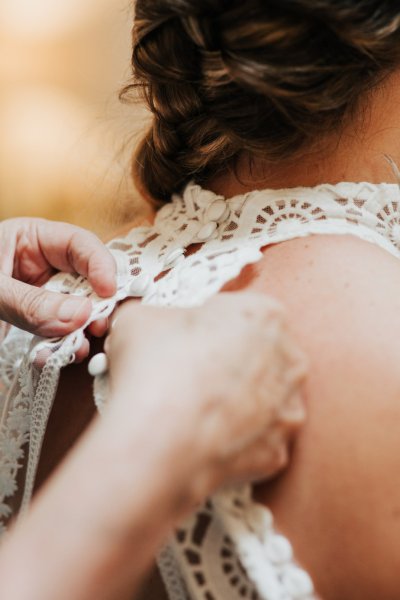 Bridesmaid helping bride button up lace dress