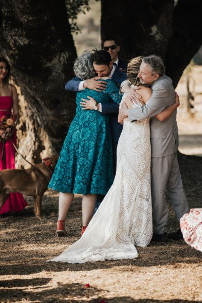 Mother hugs groom father hugs bride at wedding aisle