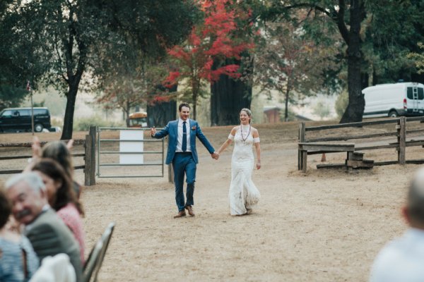 Bride and groom holding hands hand in hand walking towards guests