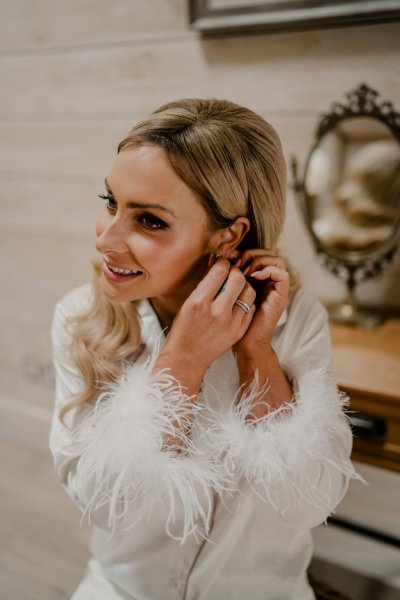 Bride putting on earrings feather arm pajamas