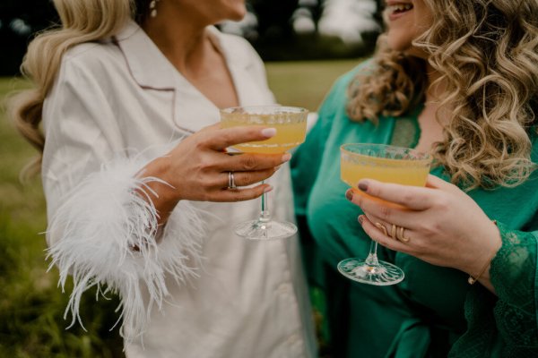 Bride and bridesmaid champagne alcohol cheers feather arms