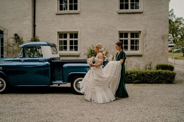 Bride outside venue train flowers bridesmaid wedding car