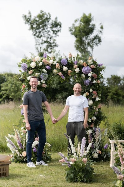 Grooms hand in hand in front of flower display wedding ceremony