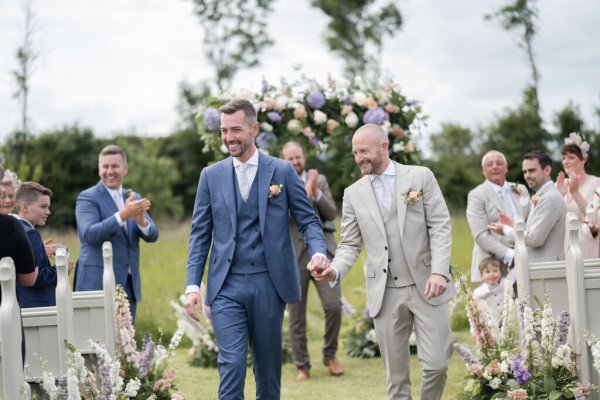 Groom and groom hand in hand flowers in background