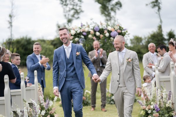 Groom and groom hand in hand flowers in background