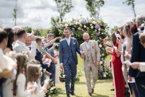 Grooms exit wedding celebrate just wed flowers holding hands