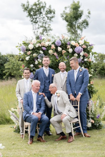 Family portrait grooms groomsmen flowers in background roses