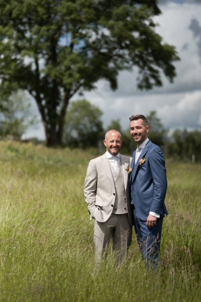 Grooms standing in field beside farm