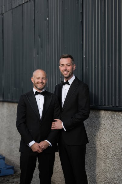 Grooms standing beside farm house