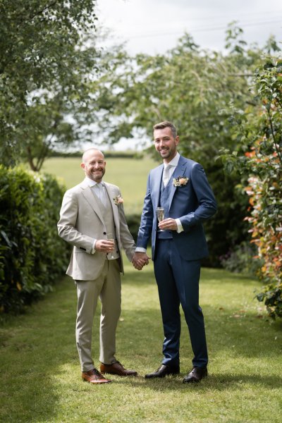 Groom and groom standing on grass holding hands