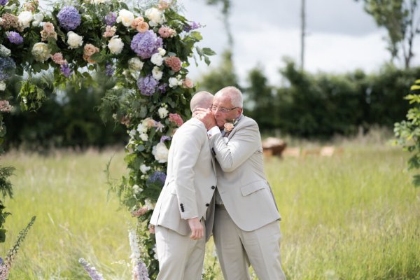 Groom and groom hand in hand flowers in background father