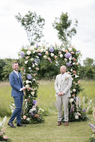 Groom and groom hand in hand flowers in background