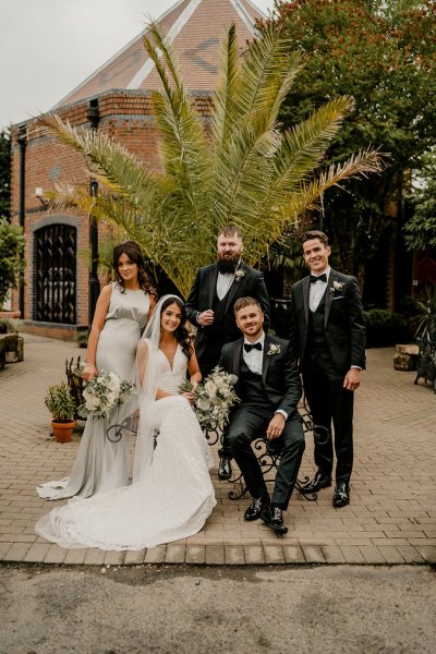 Bride groom groomsmen and bridesmaid sit on bench