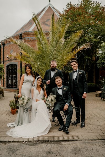 Bride groom groomsmen and bridesmaid sit on bench