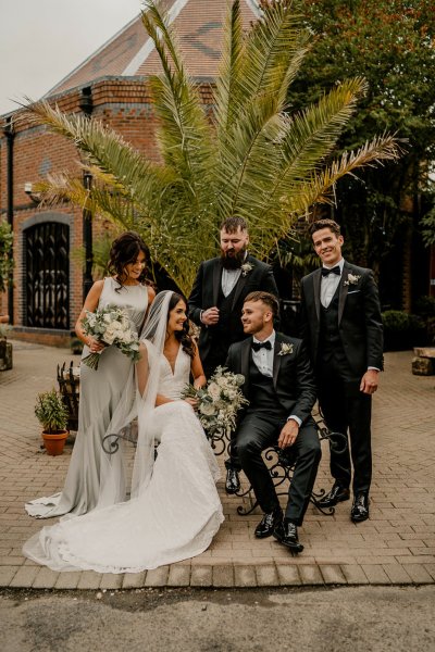 Bride groom groomsmen and bridesmaid sit on bench