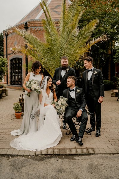 Bride groom groomsmen and bridesmaid sit on bench