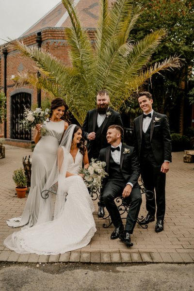 Bride groom groomsmen and bridesmaid sit on bench