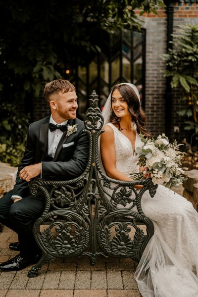 Bride and groom sit on bench looking at each other