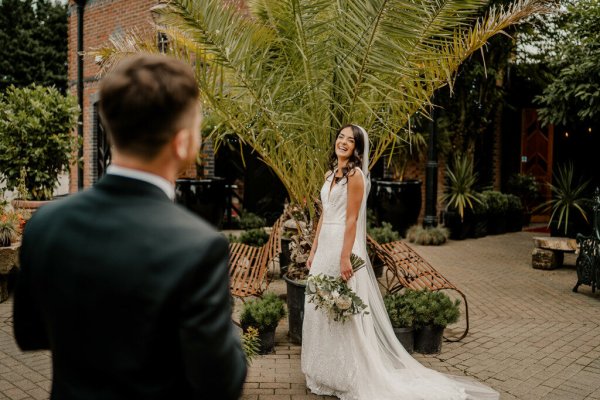 Tree in background bride on her own flowers by her side groom in shot laughing