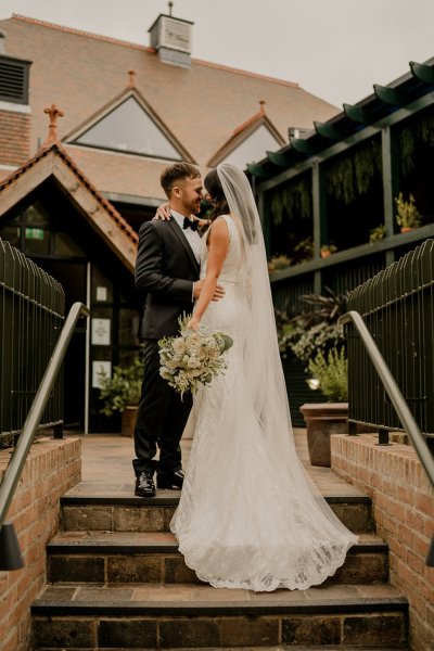 Bride and groom hand in hand holding hands carrying bouquet of flowers on steps