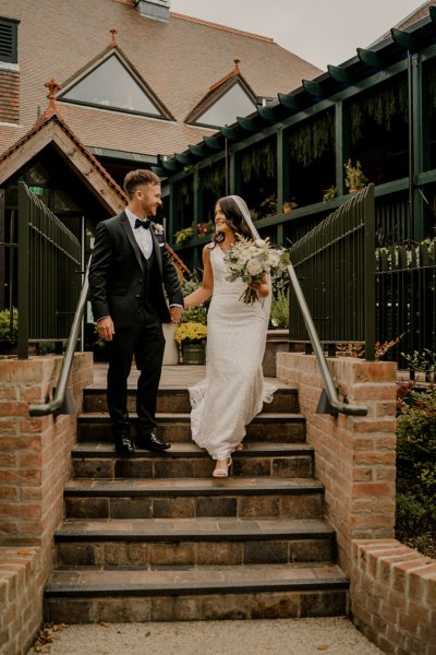 Bride and groom hand in hand holding hands carrying bouquet of flowers walking down steps