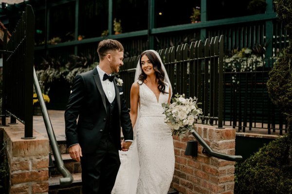 Bride and groom hand in hand holding hands carrying bouquet of flowers