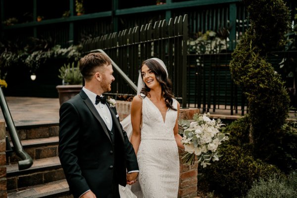 Bride and groom hand in hand holding hands carrying bouquet of flowers