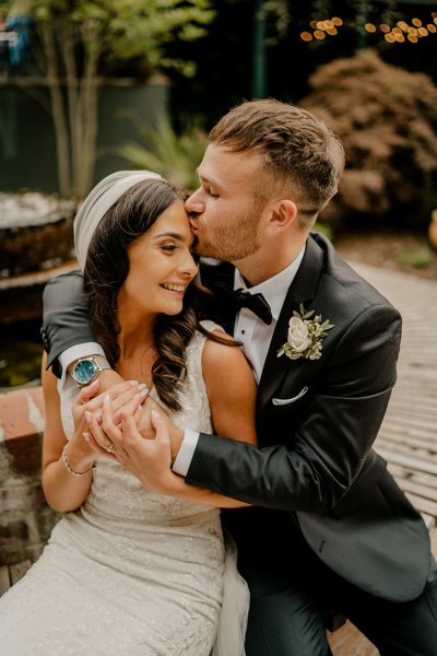 Groom kisses bride on forehead shes wearing a veil