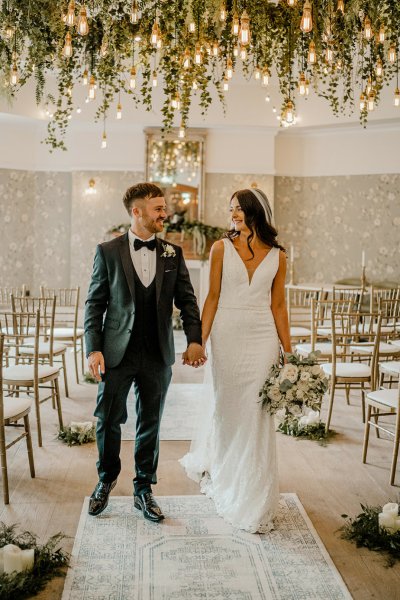 Bride and groom in empty wedding ceremony room holding hands