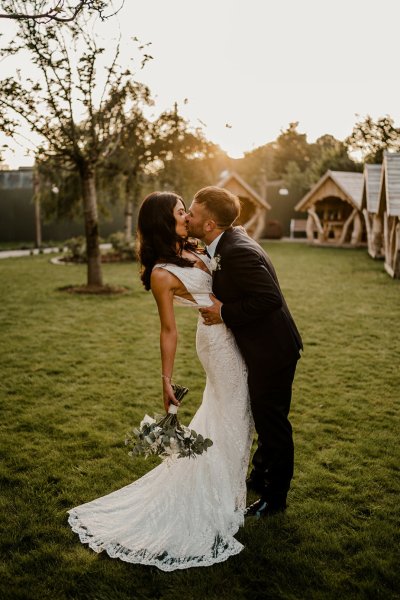 Bride bends back as groom plants a kiss holding flowers