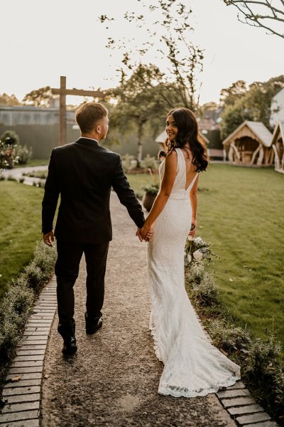 Bride looks over shoulder walking hand in hand with groom