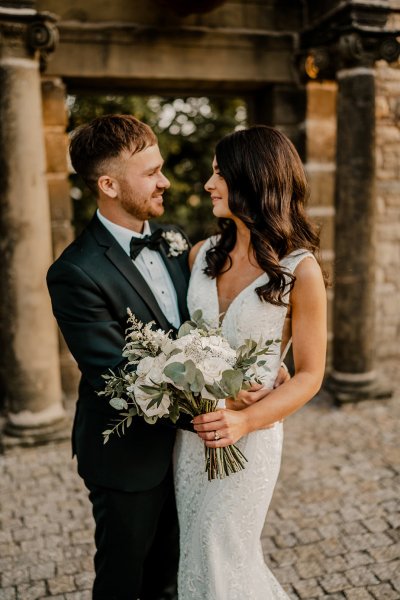 Bride and groom exterior autumn shot look at each other white flowers