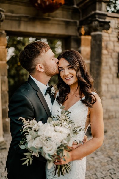 Groom kisses bride on forehead white flowers