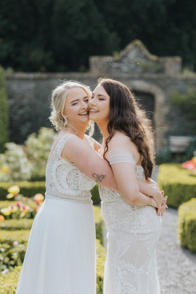 Brides in garden sunshine hug laugh flowers