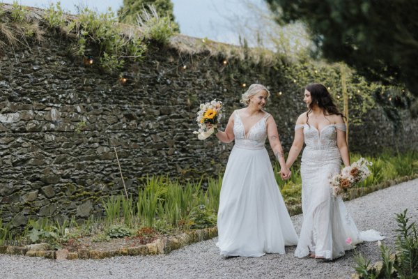 Brides walking holding flowers hand in hand wall in background