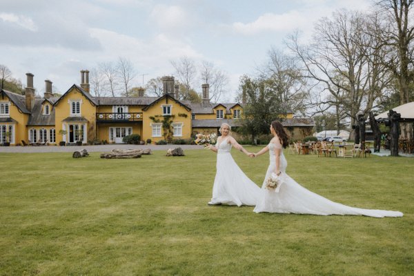 Brides wives walking through field with flowers bouquet venue in background