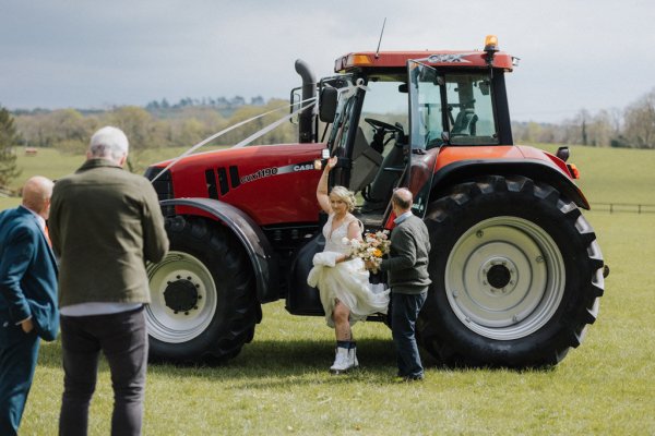 Bride gets out of tractor holding bouquet of flowers