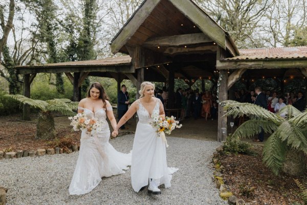 Brides hand in hand walking holding flowers