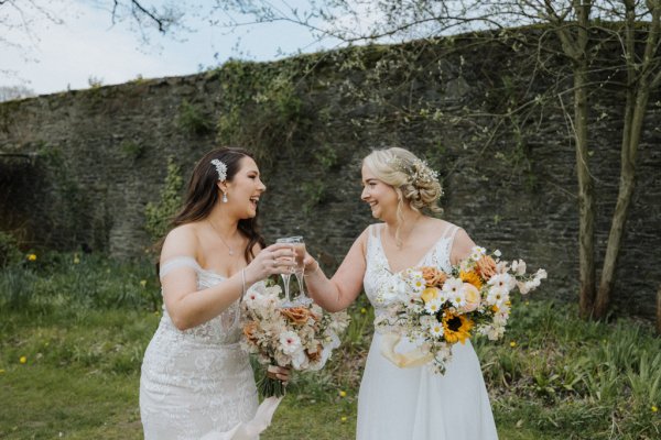 Two brides cheers with glass of champagne prosecco couple daisies flowers bouquet