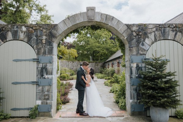 Bride and groom kiss under arch venue