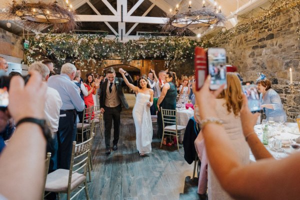 Couple hand in hand enter ceremony room with guests bride groom