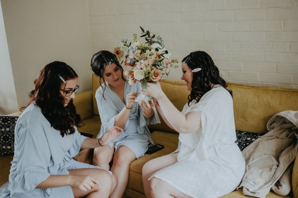 Bride and bridesmaids admire bouquet of flowers bridalwear