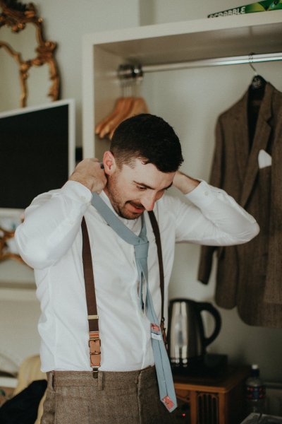 Groom wearing suspenders and white shirt getting ready