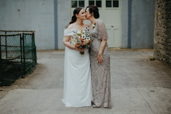 Mother and daughter bride pose with flowers kiss on the cheek