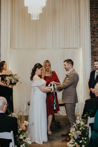 Bride with groom at alter priest ceremony bound ribbon