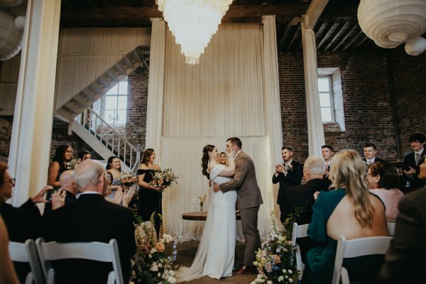 Bride with groom at alter priest ceremony kiss kissing guests clapping