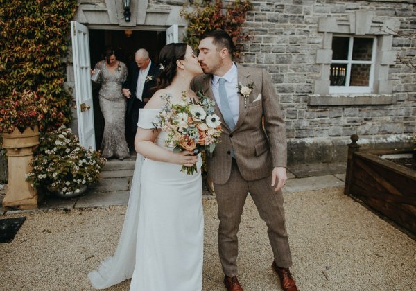 Bride and groom kiss outside of church holding flowers