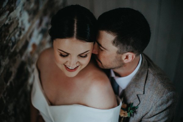 Groom kisses bride on neck close